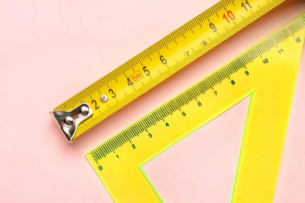 Measuring tape and triangle ruler on pink background