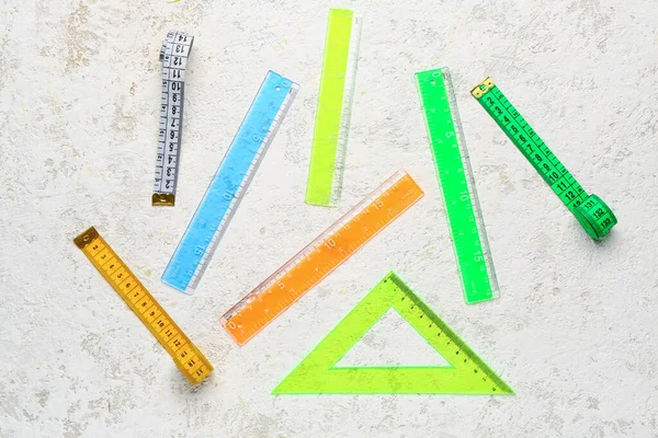 Colorful plastic rulers and measuring tapes on light grunge background