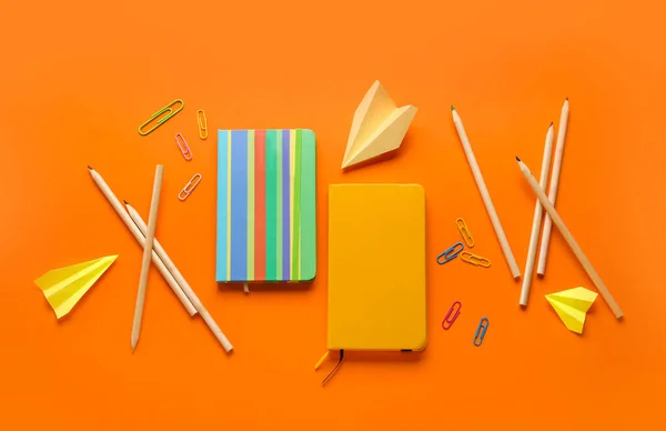 Composition with, notebooks stationery supplies and paper plane on orange background