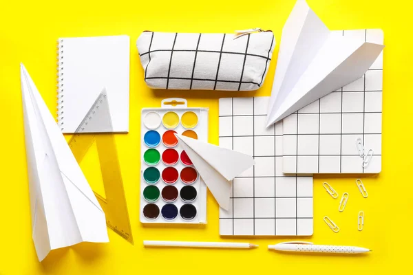 Composition with paints, notebooks and paper planes on yellow background