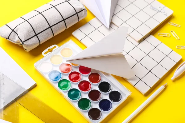 Composition with paints, notebooks and paper planes on yellow background