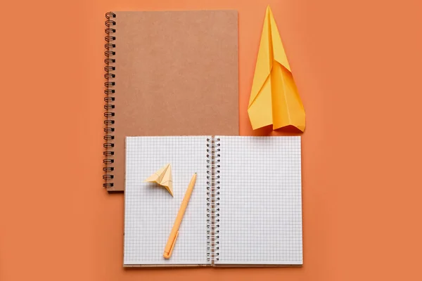 Composition with notebooks and paper planes on orange background