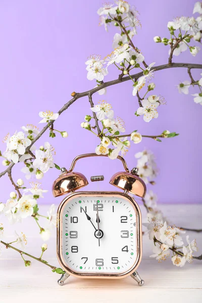 春の枝を開花し 紫色の壁の近くの白い木製のテーブルの目覚まし時計 — ストック写真