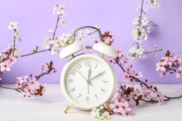 Blühende Frühlingszweige Und Wecker Auf Weißem Holztisch Neben Lila Wand — Stockfoto