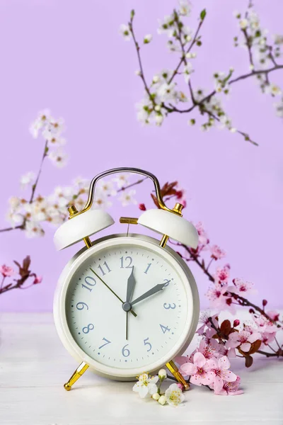 Цветущие Весенние Ветви Будильник Белом Деревянном Столе Возле Фиолетовой Стены — стоковое фото