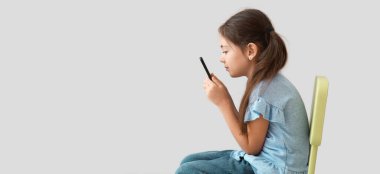 Little girl with bad posture using mobile phone on light background clipart