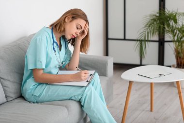 Modern klinikteki kanepede oturan yorgun kadın doktor asistanı.