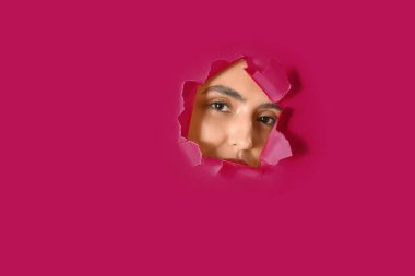Pembe kağıttaki delikten görünen genç bir kadın.