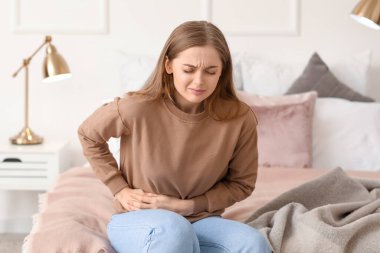 Evde yatakta oturan apandisiti olan genç bir kadın.