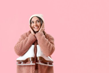 Pretty young woman with ice skates on pink background