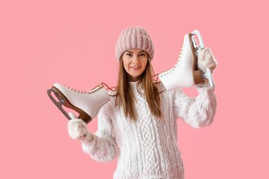 Pretty young woman with ice skates on pink background