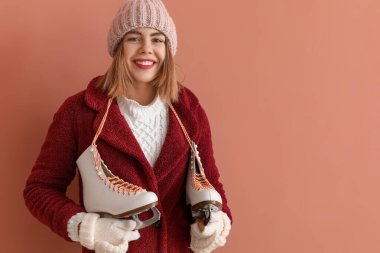 Pretty young woman with ice skates on pink background