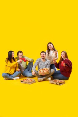 Sarı arka planda lezzetli pizza ve içecekler olan bir grup arkadaş.
