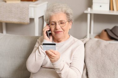 Kredi kartıyla evdeki koltukta cep telefonuyla konuşan yaşlı bir kadın.