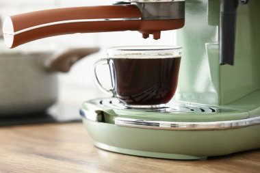 Ahşap mutfak tezgahında bir fincan espresso ile modern kahve makinesi, yakın plan.