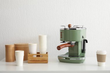 Modern kahve makinesi ve bardaklar beyaz duvarın yanındaki masada.