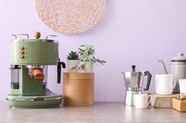 Modern kahve makinesi, fincanlar, ev bitkileri ve leylak duvarın yanındaki masada çaydanlık.