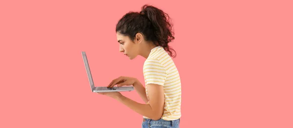 在粉色背景下使用笔记本电脑的姿势不好的年轻女人 — 图库照片