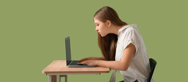 十代の女の子とともに悪いです姿勢とともにラップトップを使用してテーブルに座っています緑の背景 — ストック写真