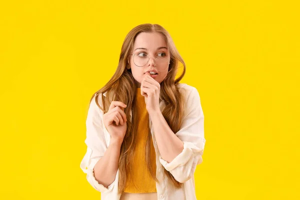 若いです女性で眼鏡かむ爪上の黄色の背景 — ストック写真