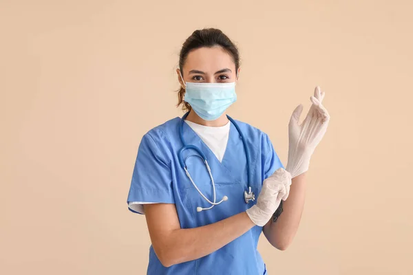 Kvinna Medicinsk Assistent Sätta Gummihandskar Mot Beige Bakgrund — Stockfoto