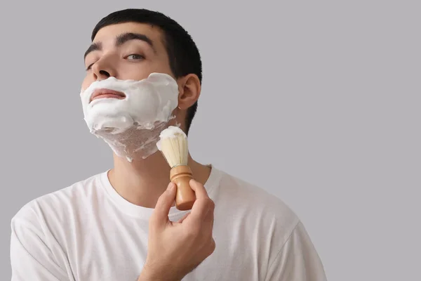Jovem Aplicando Espuma Barbear Rosto Contra Fundo Claro — Fotografia de Stock