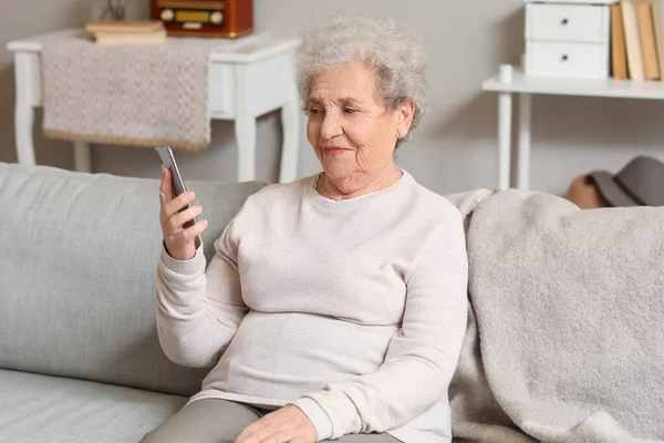 Senior woman with mobile phone video chatting on sofa at home