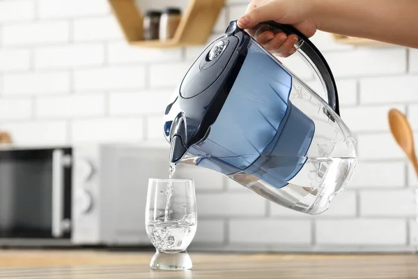 Woman pouring water from filter jug into glass on kitchen counter