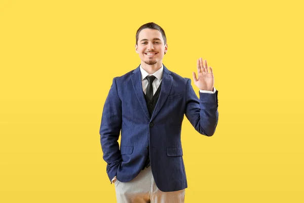 Handsome businessman waving hand on yellow background