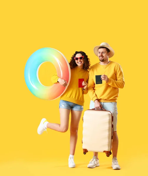 黄色の背景にパスポート インフレータブルリングとスーツケースを持つ若いカップル — ストック写真