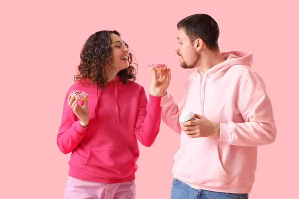年轻夫妇 有美味的甜甜圈和粉色背景的咖啡 — 图库照片