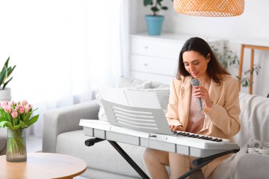 Genç bayan müzisyen evde sentezleyici çalıyor ve şarkı söylüyor.