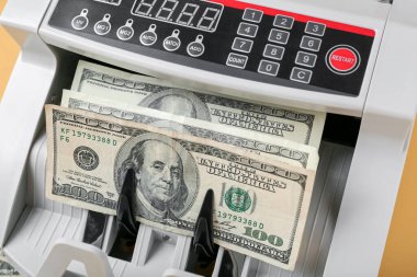 Sarı arka planda dolar banknotları olan modern para sayma makinesi, yakın plan