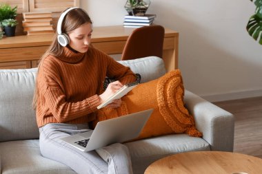 Not defteri olan kız öğrenci evdeki kanepede ders çalışıyor.