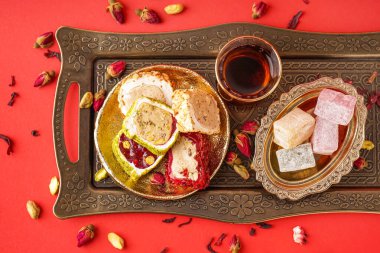 Lezzetli Türk tatlısı tepsi ve kırmızı arka planda bir bardak çay