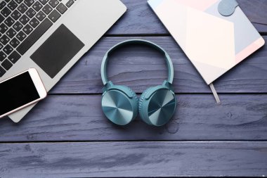 Koyu ahşap arka planda cep telefonu, dizüstü bilgisayar ve not defteri olan kulaklıklar.