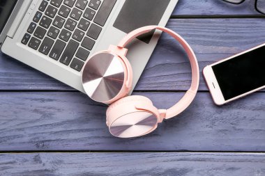 Koyu ahşap arka planda cep telefonu ve dizüstü bilgisayarı olan kulaklıklar