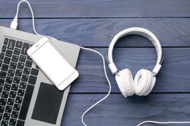 Koyu ahşap arka planda cep telefonu ve dizüstü bilgisayarı olan kulaklıklar