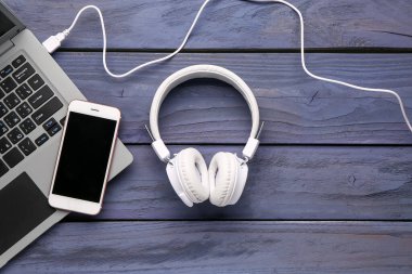 Koyu ahşap arka planda cep telefonu ve dizüstü bilgisayarı olan kulaklıklar