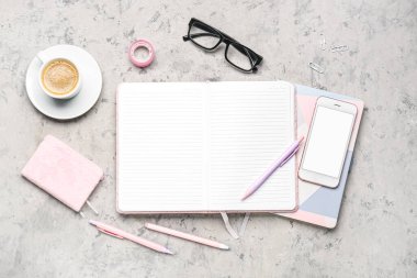 Not defteri, cep telefonu, kalemler, bardaklar ve gri masadaki kahve fincanı ile kompozisyon