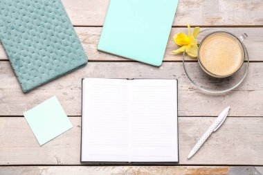 Defterli kompozisyon, yapışkan not, bir fincan kahve ve yıpranmış ahşap masa üzerindeki narsist çiçek.