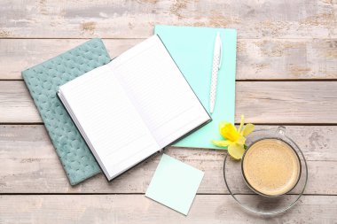 Defterli kompozisyon, yapışkan not, bir fincan kahve ve yıpranmış ahşap masa üzerindeki narsist çiçek.