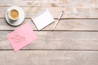 Kompozisyon defteri, zarf ve bir fincan kahve yıpranmış ahşap masada.