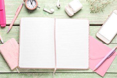 Yeşil ahşap masa üzerinde defter, cep telefonu, saat ve kulaklıkla kompozisyon