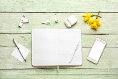 Yeşil ahşap masada defter, cep telefonu, kulaklık ve USB flaş bellekli kompozisyon