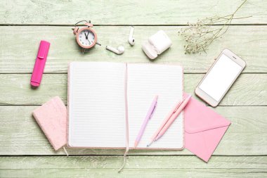 Yeşil ahşap masa üzerinde defter, cep telefonu, saat ve kulaklıkla kompozisyon
