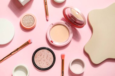 Makyaj fırçaları ve pembe arka planda podyumlarla dekoratif kozmetik ürünler.
