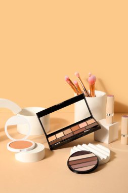Bej arka planda fırçalar ve podyumlarla dekoratif kozmetik ürünler