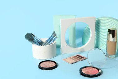 Mavi arka planda fırçalar ve podyumlarla dekoratif kozmetikler