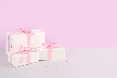 Güzel fiyonklu hediye kutuları ve pembe arka planda konfeti.